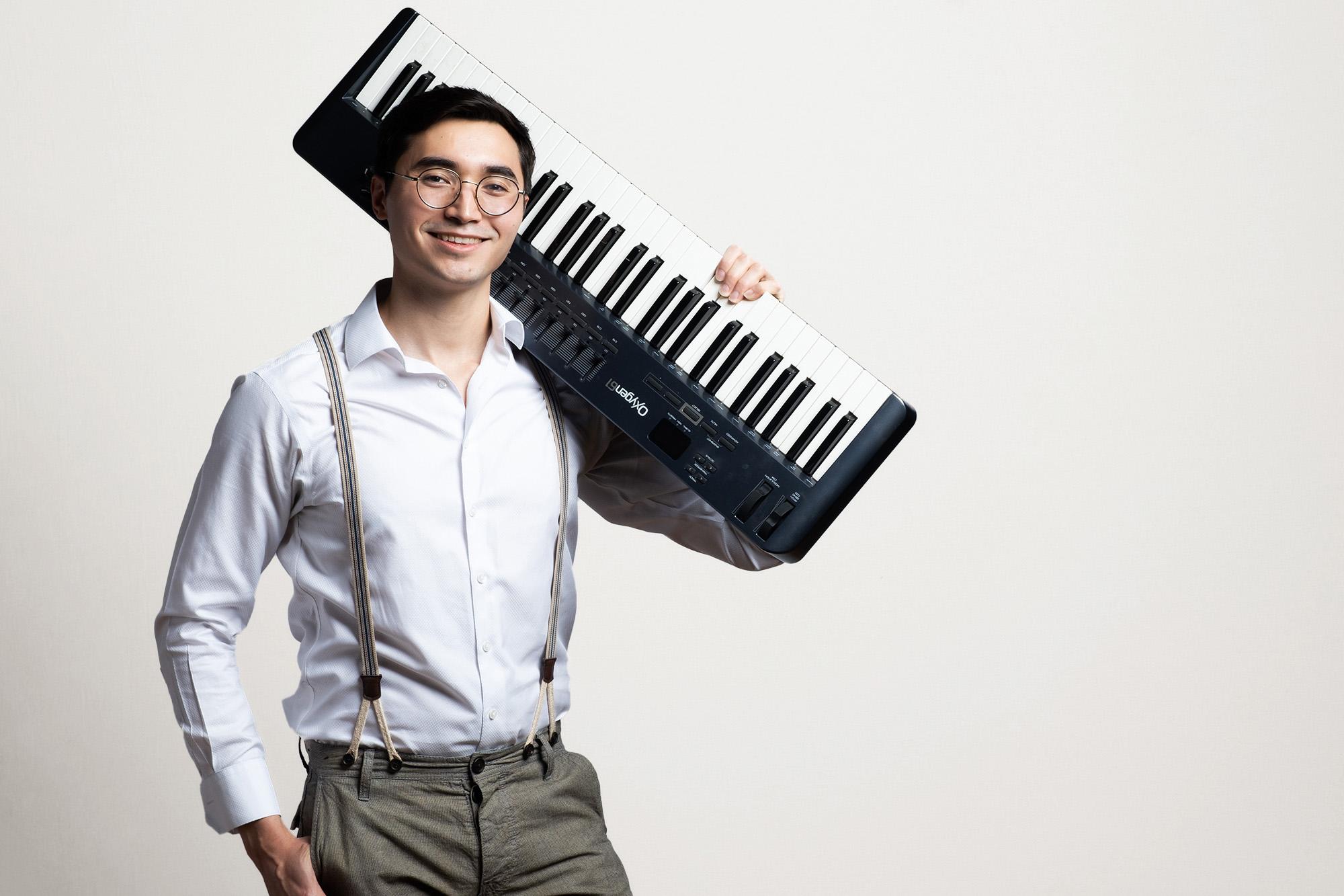 Student Composer looks into camera with electronic keyboard on his shoulder