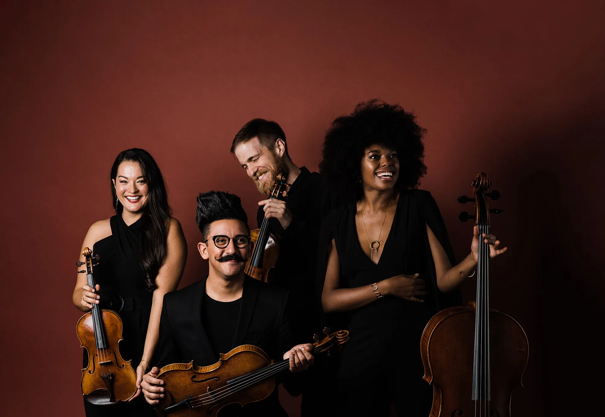 Thalea String Quartet pose with instruments in front of a red wall