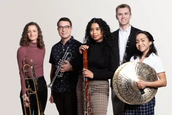 a group of Wind Ensemble students hold their instruments and look confidently at the viewer.