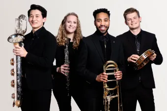 A group of Wind Symphony Students hold their instruments and look confidently at the viewer.