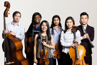 a group of students from Symphony orchestra hold their instruments and look confidently at the viewer