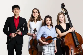 A group of students from University Orchestra hold their instruments and look confidently at the camera