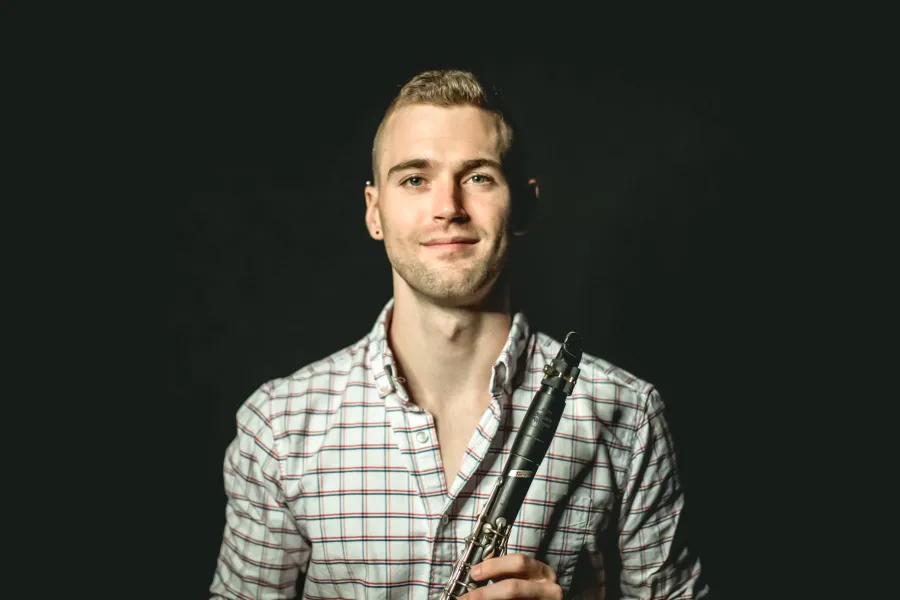A headshot of clarinetist Tyler Webster wearing a checkered shirt holding his instrument.