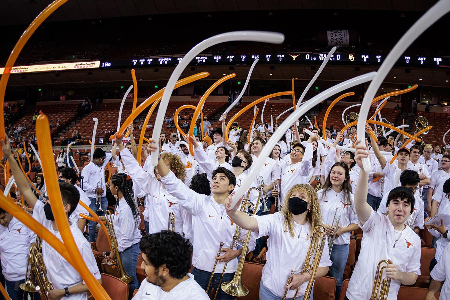 Pep Band members stand in the audience waving long burnt orange and white balloons in the air
